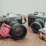 Two cameras sitting on a table with a box and a camera